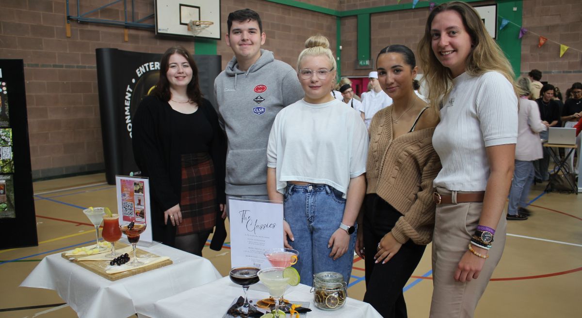 Group of five students in front of a display table of beverages